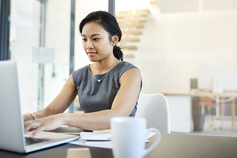 A young woman in business attire types on a laptop at a desk