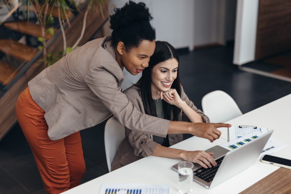 Two women look at a laptop screen in an office setting