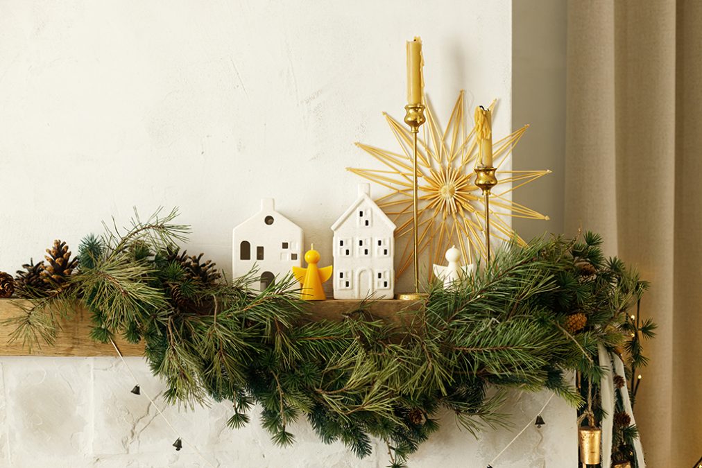 Stylish christmas decorated fireplace mantel with fir branch, candles, ceramic houses, bells, ribbon