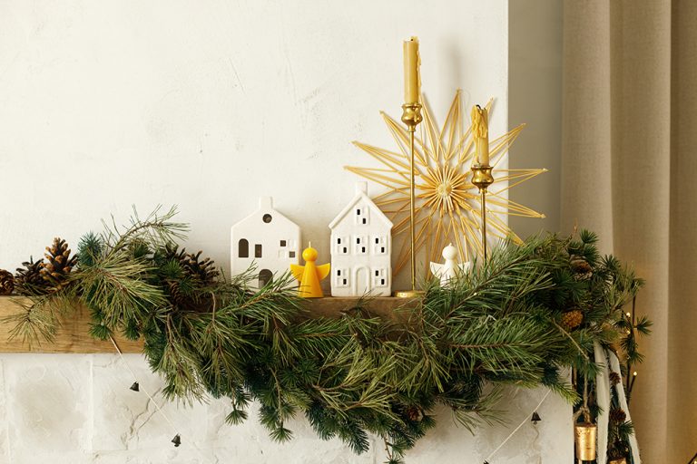 Stylish christmas decorated fireplace mantel with fir branch, candles, ceramic houses, bells, ribbon