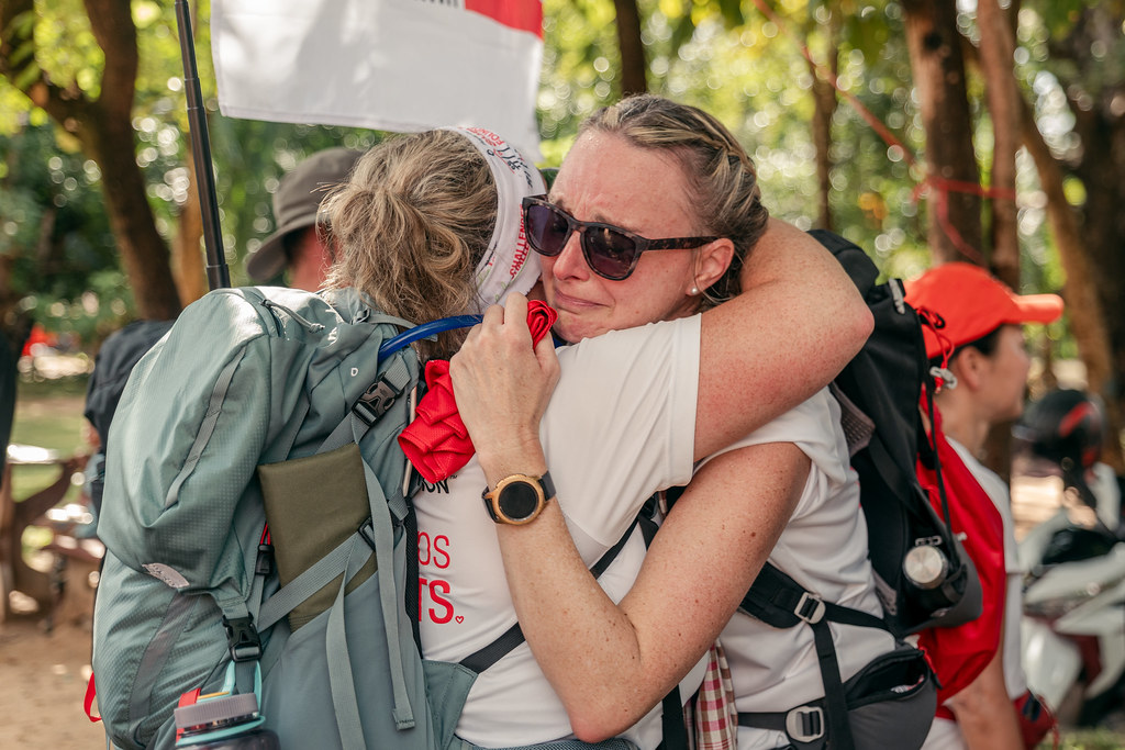 Two women in hiking attire share an emotional embrace 