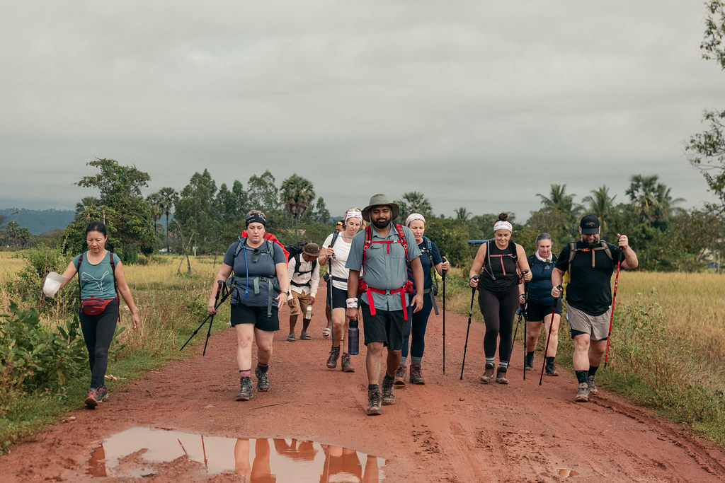A group of hikers cross a muddy trail in Cambodia