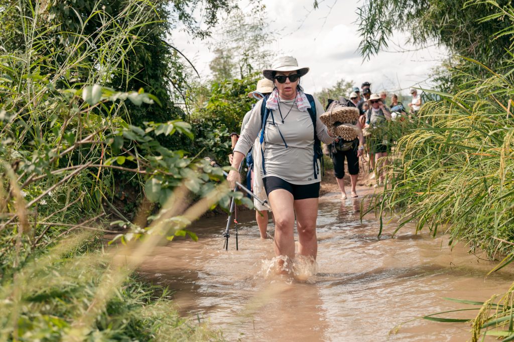 A woman in hiking attire wades through water in the Cambodian jungle 