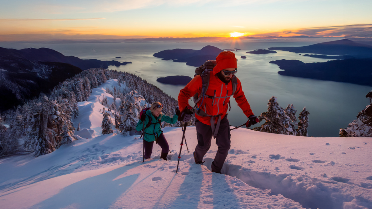 Man and woman are hiking to the top of a mountain during a vibrant winter sunset