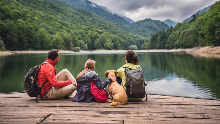 Family with a small yellow dog resting on a pier and looking at lake and foggy mountains