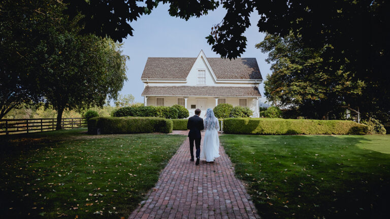 Bride and groom on their wedding day standing in front of white house on summer day
