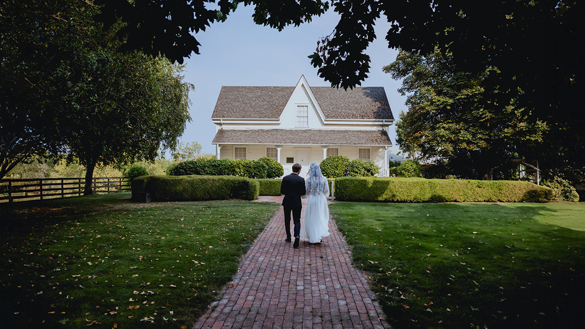 Bride and groom on their wedding day standing in front of white house on summer day