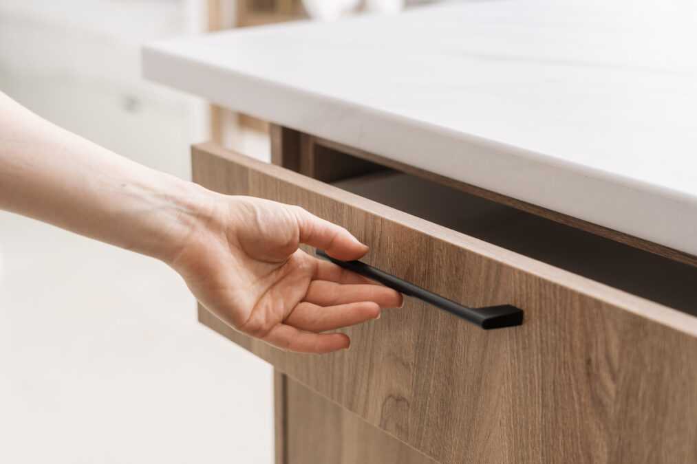 Cropped shot of woman hand is opening a wooden drawer in a contemporary kitchen with a sleek, minimalist design