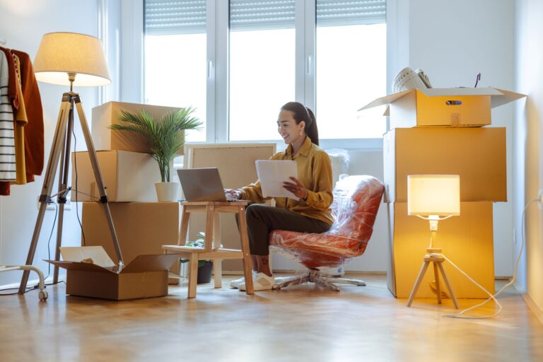 Businesswoman multitasking while working on her laptop surrounded by cardboard boxes in her new house