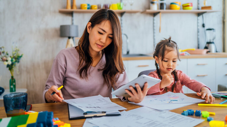 Young mother going through her financials, daughter sit nearby and playing