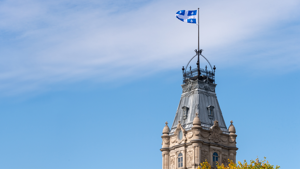 Exterior view of top of Quebec’s provincial parliament; Quebec flag flying in the sun.