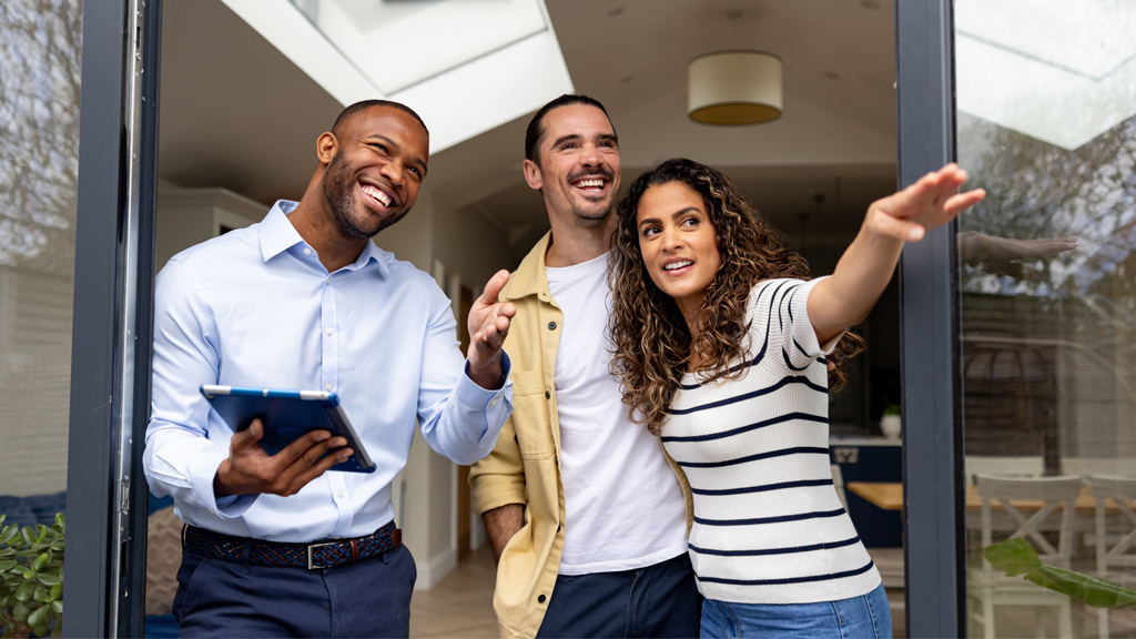 Happy real estate agent showing a couple the back yard of a house for sale through the sliding door
