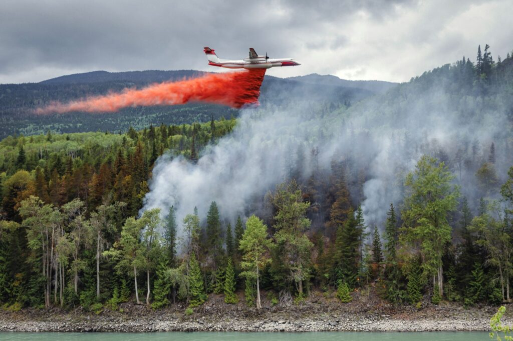 Firefighting plane releases red fire retardant over smokey forest